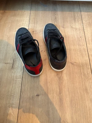 Gucci skor - Säljer mina svarta Gucci sneakers med klassiskt GG-mönster. De har röda och blå ränder på sidorna och röd samt blå detalj i ormskinn-look på hälen. Tillverkade i skinn och textil, med Gucci-märkning både på insidan och undersidan. Följer med ett par extra Gucci-skosnören (oanvända). Storlek 40-41 (amerikansk storlek 6 1/2). Skorna är i mycket bra skick, använda varsamt ca 5 gånger. Köpta på Guccibutiken på Birger Jarls Gatan i Stockholm för 8 000 kr.