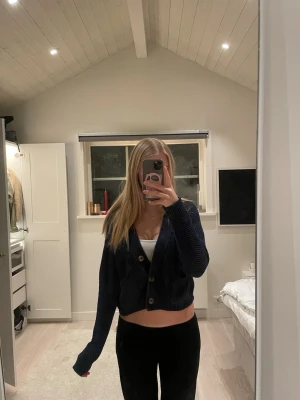 Mörkblå croppad kofta med knappar - Säljer en mörkblå croppad kofta med stora knappar framtill. Koftan är stickad i ett mjukt material och har långa ärmar samt två fickor framtill. Är storlek xxs men passar mig som är S 