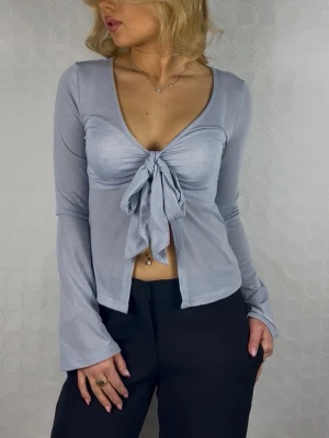 Ljusblå långärmad topp med knyt - Supersnygg ljusblå långärmad topp från Bershka med djup v-ringning och knyt framtill. Toppen är croppad och har en mjuk, stretchig känsla. Perfekt att styla med höga byxor för en trendig look.