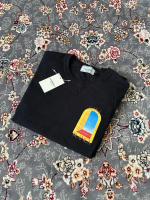 Svart Casablanca t-shirt med färggrafik - Svart t-shirt från Casablanca med stor färgglad grafik i gult, blått och rött både fram och bak. Klassisk rund hals och korta ärmar. Mjuk bomullskvalitet och clean vibe, perfekt för dig som gillar streetwear med en twist.