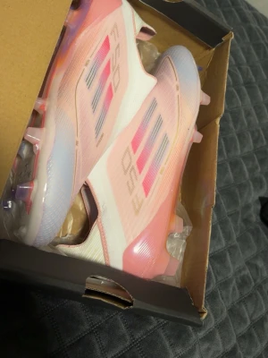 Lamine yamal edition,Adidas rosa/vita fotbollsskor - Säljer ett par riktigt snygga Adidas fotbollsskor i vitt och ljusrosa med lila detaljer. Skorna har en strömlinjeformad design, plastdobbar och coola detaljer under sulan. Ovandelen är i syntetmaterial och har de klassiska tre ränderna på sidan.