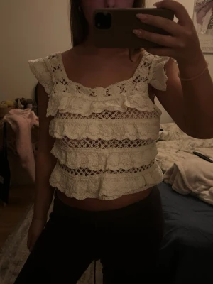 Vit spetsblus med volanger - Säljer en superfin vit blus i spets med flera lager volanger och genombrutet mönster. Toppen kan bäras både på axlarna och offshoulder för olika looks. Den har korta volangärmar och är croppad i modellen. Perfekt för dig som gillar romantisk och bohemisk stil.