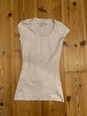 Ljusrosa t-shirt från H&M L.O.G.G. - En basic ljusrosa t-shirt från H&M L.O.G.G. i ekologisk bomull. Modellen är figurnära med korta ärmar och rund halsringning. Liten broderad detalj nertill på framsidan. Perfekt till jeans eller shorts för en chill look. Den har en liten blå fläck som man ser på bilden