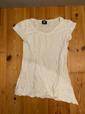 Vit kortärmad topp från Wear It - Enkel vit topp från Wear It med rund halsringning och korta ärmar. Lätt och luftig modell i mjuk bomull, perfekt till sommaren. Liten rynkdetalj i midjan för en snyggare passform.