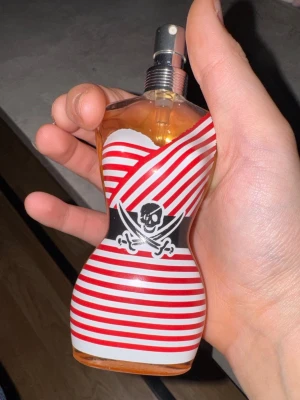 Jean paul gaultier la male pirate. Typ 55/60ml kvar  - Unik parfymflaska i form av en kropp med röda och vita ränder samt piratmotiv. Perfekt för dig som gillar statement-detaljer på hyllan. Märket är känt för sina kreativa designer.Tyvärr ingen box. Pris kan diskuteras 