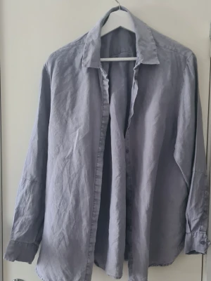 Ljusgrå oversized skjorta i linne - Säljer en ljusgrå oversized skjorta i linne med klassisk krage och långa ärmar. Märke Wera (Åhléns). Skjortan har knappar framtill och en avslappnad passform som ger en chill vibe. Perfekt att bära öppen över ett linne eller stängd för en clean look.