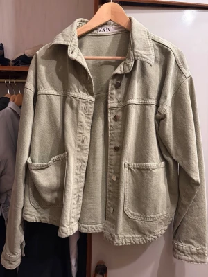 Grön jeansjacka från Zara - Säljer en grön jeansjacka från Zara i storlek S. Jackan har klassisk krage, stora framfickor och knappar framtill. Perfekt att slänga över en hoodie eller t-shirt för en chill look.
