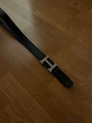 H bälte  - svart bälte med ett stort H-format metallspänne. Står inte vilken märke. Tror bältet är 110cm långt 