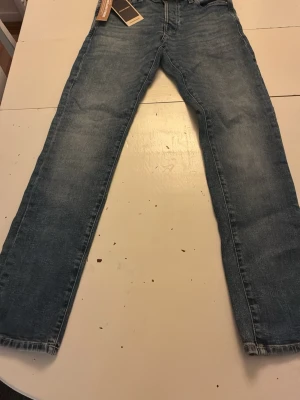 Jack & Jones Slim Glenn blå jeans - Säljer ett par Slim Glenn jeans från Jack & Jones i klassisk blå denim. Modellen har låg midja, smal passform över lår och knä samt tight benslut. Jeansen är tillverkade i stretchigt material för extra komfort ochför en avslappnad look, aldrig andvända.