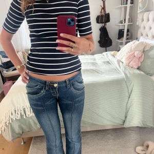 Lågmidjade blå bootcut jeans - Säljer ett par blå lågmidjade jeans med bootcut-snitt och snygga detaljerade fickor. Jeansen har markerade sömmar framtill och cool grön brodyr på bakfickan. Perfekta för dig som gillar en retro vibe och vill sticka ut lite extra. Skulle säga att de passar en 36 eller 38 💕💕