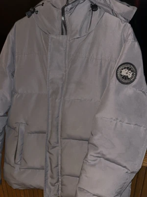 Canada Goose Jacka - Canada Goose Macmillan Parka jacka i storlek M, passar även S. färg grå/graphite,  Jackan är köpt i London för 2 år sedan och jag säljer den eftersom jag har köpt en annan vinterjacka och denna står bara i garderoben. Tillverkad i polyester. Jackan är avsedd för utomhusbruk och har en design som erbjuder värme och skydd mot väderförhållanden.