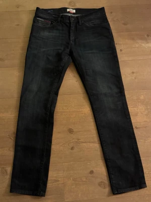 Mörkblå slim jeans Tommy Hilfiger - Säljer ett par mörkblå slim fit jeans från Hilfiger Denim. Klassisk femficksmodell med snygga detaljer och diskret logga på myntfickan. Jeansen har raka ben och är tillverkade i ett mjukt jeansmaterial som sitter riktigt bra. Märkena på baksidan av benen är catchiga och ger jeansen en extra detalj, men borde med största sannolikhet gå bort i tvätten. Storlek 32/32!