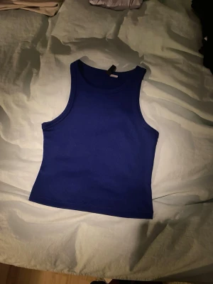 Blå ribbad linnetopp från Divided - Säljer en enkel och snygg blå linnetopp från Divided by H&M i storlek S. Toppen är ribbad och har en klassisk ärmlös design med rund halsringning. Perfekt att matcha med jeans eller kjol för en clean look.