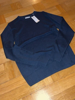 Mörkblå stickad tröja Jack & Jones - Snygg mörkblå stickad tröja från Jack & Jones i klassisk modell med rund hals och ribbade muddar. Perfekt till höst och vinter, enkel att matcha med jeans eller chinos. Materialet är mjukt och skönt, passar dig som gillar stilrena plagg.