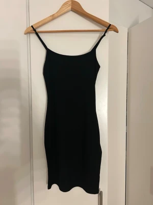 Svart ribbad klänning från new yorker - Säljer en svart ribbad kortklänning med smala, justerbara axelband. Klänningen har en enkel och stilren design som sitter figurnära och är perfekt för dig som gillar minimalistisk stil. Bara testad och inte använd! 