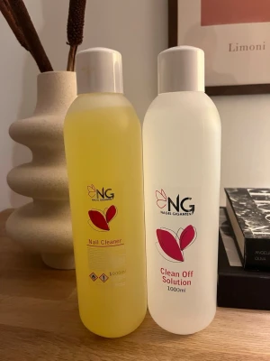 Nagel Giganten Nail Cleaner & Clean Off - Två stora flaskor från Nagel Giganten, en Nail Cleaner (gul vätska) och en Clean Off Solution (klar vätska), båda på 1000 ml. Perfekt för att rengöra naglar och ta bort kladd från gel eller akryl. Snygg design med röda blad på etiketten.