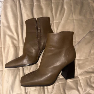 Mörkbruna klackskor - Snygga bruna stövletter i skinn med hög klack. Dragkedja på insidan för enkel på- och avtagning. Stilren design med slät yta och fyrkantig form framtill. Använda fåtal gånger och i bra skick. 8 cm klack.