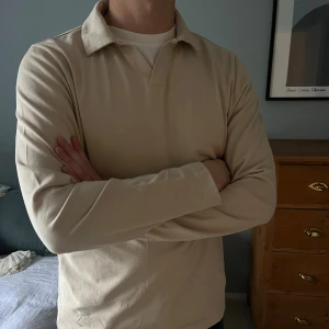 Beige långärmad pikétröja A Day’s March - Snygg beige pikétröja från A Day’s March med klassisk krage och lång ärm. Tröjan är tillverkad i mjuk bomull och har en stilren, enkel design utan mönster eller detaljer. Perfekt som overshirt. Modellen heter ”Branford Long Sleeve Jersey Polo” NYPRIS: 795