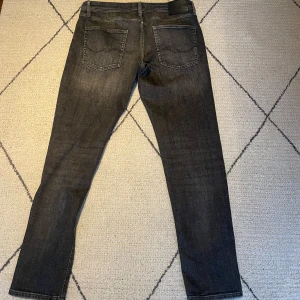 Svarta slim jeans från Jack & Jones 34/34 - Snygga svarta jeans från Jack & Jones med klassisk femficksdesign och smal passform. Jeansen har en mörk tvätt med subtila slitningar och raka ben. 