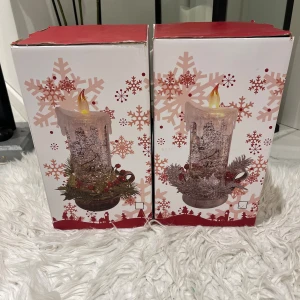 LED Dekorationsljus Jul - Två LED-dekorationsljus i juldesign, levereras i originalförpackning. Ljusen har glittrande effekt, konstgjord låga och dekorationer med granris och röda bär. Perfekt för julstämning. Kartongerna har mindre slitage i hörnen men är i gott skick.