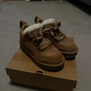 UGG LOWMEL - Säljer ett par bruna Ugg lowmel, jätte fint skicka, inte använt, mönstrade snören och fluffigt vitt runt kanten. För dig som vill ha något extra till höst och vinter.