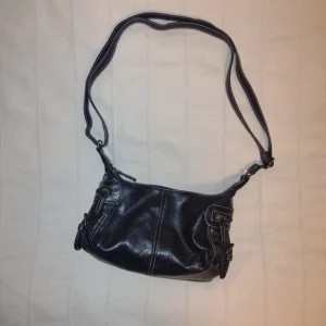 Svart Y2K väska/axelremsväska I fakeskinn  - Skitsnygg svart axelväska i konstskinn med justerbar rem och flera dragkedjefickor. Perfekt storlek för att bära med sig det viktigaste och passar till många olika stilar. Ca 23 cm lång i botten och ca 15 cm hög. I fint använt skick.