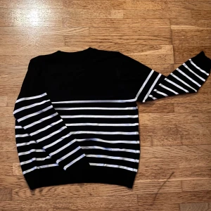 Navy vit randig stickad tröja - Snygg svart/navy blue stickad tröja med vita horisontella ränder över hela kroppen och ärmarna. Tröjan har rund hals och långa ärmar, perfekt för dig som gillar klassisk stil med en modern twist. Materialet är mjukt och bekvämt, passar till många olika outfits.