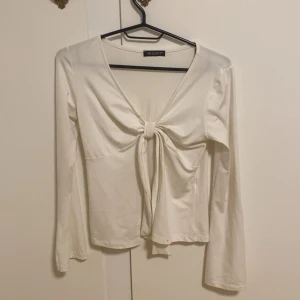 Vit långärmad topp med knyt från Missay - Säljer en vit långärmad topp från Missay med snygg v-ringning och knyt framtill. Toppen har en croppad passform och är tillverkad i mjuk bomull. Perfekt för dig som gillar stilrena och trendiga plagg med lite extra detalj. Pris kan diskuteras