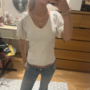 Vit ribbad topp med puffärm från ONLY - Säljer en vit ribbad topp från ONLY med korta puffärmar och v-ringning. Toppen har öppen rygg med snygg knyt-detalj bak. Pris kan alltid diskuteras!!🥰