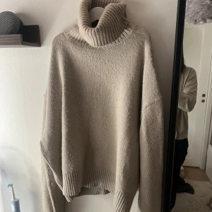 Beige polotröja med ribbad krage - Säljer en beige polotröja med bred, ribbad krage och ribbade muddar. Tröjan har en loose passform och är stickad i ett mjukt material som känns skönt mot huden. Perfekt för dig som gillar chill och oversized stil.