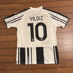 Juventus Yildiz 10 Adidas fotbollströja S - Juventus matchtröja med Yildiz och nummer 10 på ryggen. Adidas Aeroready slim fit, vit med svarta och rosa detaljer samt svarta ränder. Jeep och Visit Detroit tryck på bröstet, Juventus klubbmärke och tre rosa ränder på axlarna. Tillverkad i polyester.