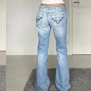 Ljusblå bootcut jeans med broderi lowwaist - Säljer ett par ljusblå bootcut jeans med snygga broderade detaljer på bakfickorna. Jeansen har låg midja och klassisk femficksdesign. 💓