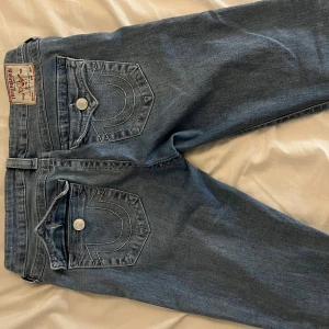 True Religion ljusblå jeans med kontrastsöm - Säljer ett par ljusblå jeans från True Religion med ikoniska kontrastsömmar och stora fickor med lock och silverfärgade knappar. Klassisk patch bak i midjan och snygg tvätt som ger en cool vibe. Perfekt för dig som gillar streetwear och detaljer. Joey modellen. Har använt bara ett fåtal gånger eftersom dom är för stora och långa.