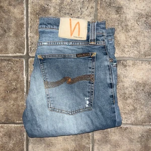 Nudie Jeans  - Blå jeans från Nudie Jeans, modell Tight Long John. Jeansen har klassisk femficksdesign, orangea sömmar och en smal passform. Tillverkade i bomull med en lätt tvättad look och diskreta slitningar. Midja 40cm, längd 106cm. Ifall det inte finns någon bild i annonsen där jag bär plaggen jag säljer så är det för att jag ej kan ha storleken heller passformen, så kolla måtten för storlek och googla på modellnamnet för passform 😉 s4