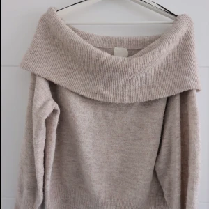 Beige offshoulder stickad tröja - Mysig beige stickad tröja med bred, ribbad offshoulder-krage. Perfekt för lager-på-lager och chill höst- eller vinterstil. Långärmad och i mjukt material som känns skönt mot huden.