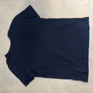 Mörkblå t-shirt från Lyle & Scott - Snygg mörkblå t-shirt från Lyle & Scott i mjuk bomull. Klassisk rund hals och korta ärmar. Diskret gul logga med fågel på nedre vänstra sidan. Perfekt basic för garderoben, enkel att matcha med allt.