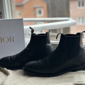 Svarta 1880 chelsea boots från Loake - Klassiska svarta  chelsea boots från Loake i slätt skinn med elastiska paneler på sidorna och dragflikar med logga. Snygg, stilren design med rund tå och robust sula som ger bra grepp. Perfekta för dig som vill ha en tidlös och clean look.