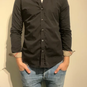 Burberry Brit svart skjorta, storlek S - Säljer en snygg svart Burberry Brit-skjorta i väldigt fint skick. Klassisk passform med diskret Burberry-detaljering och hög kvalitet i både tyg och sömnad. Inga fläckar, hål eller slitage – använd sparsamt. Storlek: S Small Nypris: ca 3-4000kr Skriv vid frågor eller ifall du vill ha fler bilder.  Kolla gärna in mina andra annonser.   