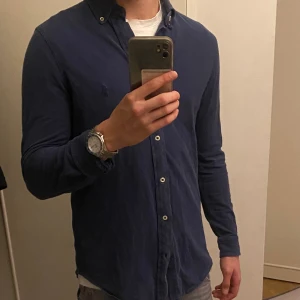 Mörkblå Ralph Lauren skjorta - Säljer en sjukt fräsch mörkblå Ralph lauren skjorta med klassisk krage och vita knappar. Skjortan har lång ärm och en slim passform som sitter snyggt på kroppen. Perfekt för dig som gillar en clean och enkel look. Han på bilden är 178 cm och den sitter på gränsen att vara för liten😇
