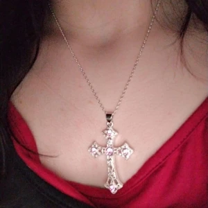 Silverfärgat halsband med kors och rosa stenar - Säljer ett snyggt halsband med ett stort kors som hänge, dekorerat med rosa glittrande stenar. Kedjan är silverfärgad och korset har detaljerad design som ger en cool vibe. Perfekt för dig som gillar statement-smycken och vill sticka ut.