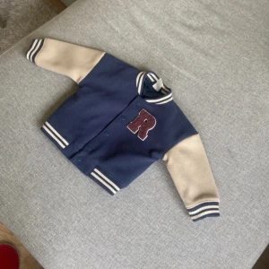 Blå bomberjacka från H&M med R - Använd 1 gång helt ny fräsch.hämtas i norsborg botkyrka eller fraktas.Snygg bomberjacka från H&M i mörkblått med beige ärmar och vita ränder på muddar och krage. Stor röd bokstav R på bröstet. Jackan har tryckknappar framtill och cool college-vibe. Perfekt för dig som gillar sportig stil.