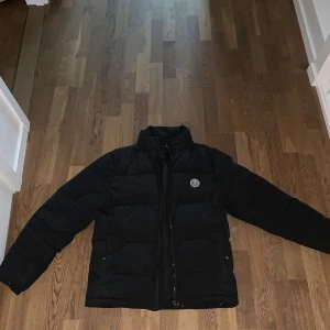 Svart Trapstar pufferjacka - Svart pufferjacka från Trapstar med broderad logga på ryggen och rund patch med 'It's a Secret' på bröstet. Perfekt för kalla dagar. ( skriv för mer bilder och jackan tvättas innan den säljs, pris kan diskuteras och luva kommer med )