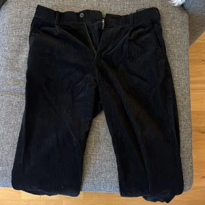 Svarta manchesterbyxor från H&M - Svarta manchesterbyxor från H&M i regular fit. Byxorna har klassisk rak passform, bälteshällor och två bakfickor med knapp. Perfekta för dig som gillar en stilren och tidlös look med lite extra textur.