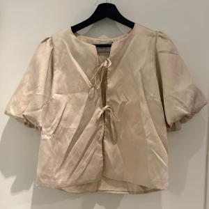 Beige blus med puffärm från Neo Noir - Säljer en beige blus från Neo Noir med korta puffärmar och två snygga knytband framtill. 😍