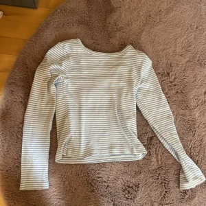 Randig långärmad topp i ljusblått - Säljer en ribbad långärmad topp från C i storlek 134/140. Toppen har ett klassiskt randigt mönster i ljusblått och vitt, rund halsringning och mjukt bomullsmaterial som är skönt mot huden. Perfekt för dig som gillar enkel och fräsch stil.