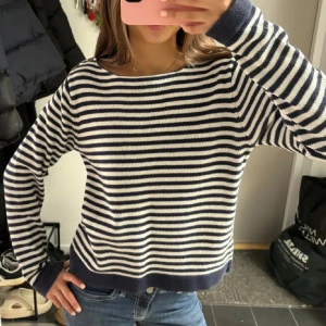 Randig stickad tröja  - Säljer en snygg stickad tröja med marinblå och vita ränder. Tröjan har en avslappnad passform, rund halsringning och långa ärmar med breda muddar. Perfekt för dig som gillar en klassisk och chill stil.