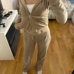 Beige Juciy Couture set - Juciy set som använts några gånger. Har lite skador som för de mesta bara är smuts men också kan vara små slitningar på både byxorna och koftan men inga större tecken. Det är också bara ena snöret som syns. Pris kan diskuteras!