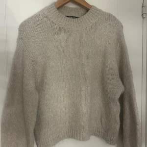 Beige stickad tröja Gina Tricot - Mysig beige stickad tröja från Gina Tricot i storlek XS. Tröjan har en rundad, ribbad hals och långa ärmar. Den är fluffig och har en loose passform som ger en chill vibe. Perfekt för att hålla sig varm under kyliga dagar.