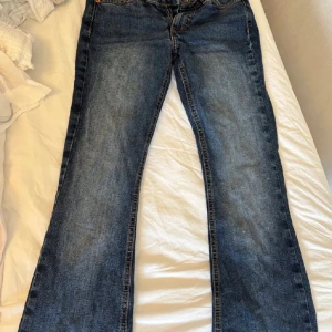 Blå low waisted bootcut jeans från Junkyard - Snygga blå bootcut jeans från Junkyard med klassisk femficksdesign och coola kontrastsömmar på bakfickorna. Jeansen är low waisted. Jeansen har normal passform och är tillverkade i slitstarkt denim med en mörk tvätt. Perfekt för dig som gillar retrovibbar och vill sticka ut.
