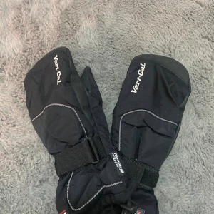 Svarta snowboardvantar från Vert-Cal - Säljer ett par svarta snowboardvantar från Vert-Cal med Twin-Unit system och Thinsulate-foder. Vantarna har justerbara band runt handleden, förstärkta partier och vita sömmar som detalj. Perfekta för kalla vinterdagar i backen.